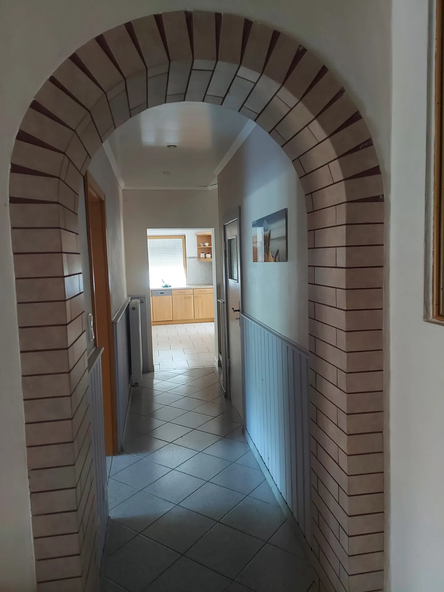 Flur mit gemauertem Rundbogen und Fliesenboden, Blick bis in die Küche