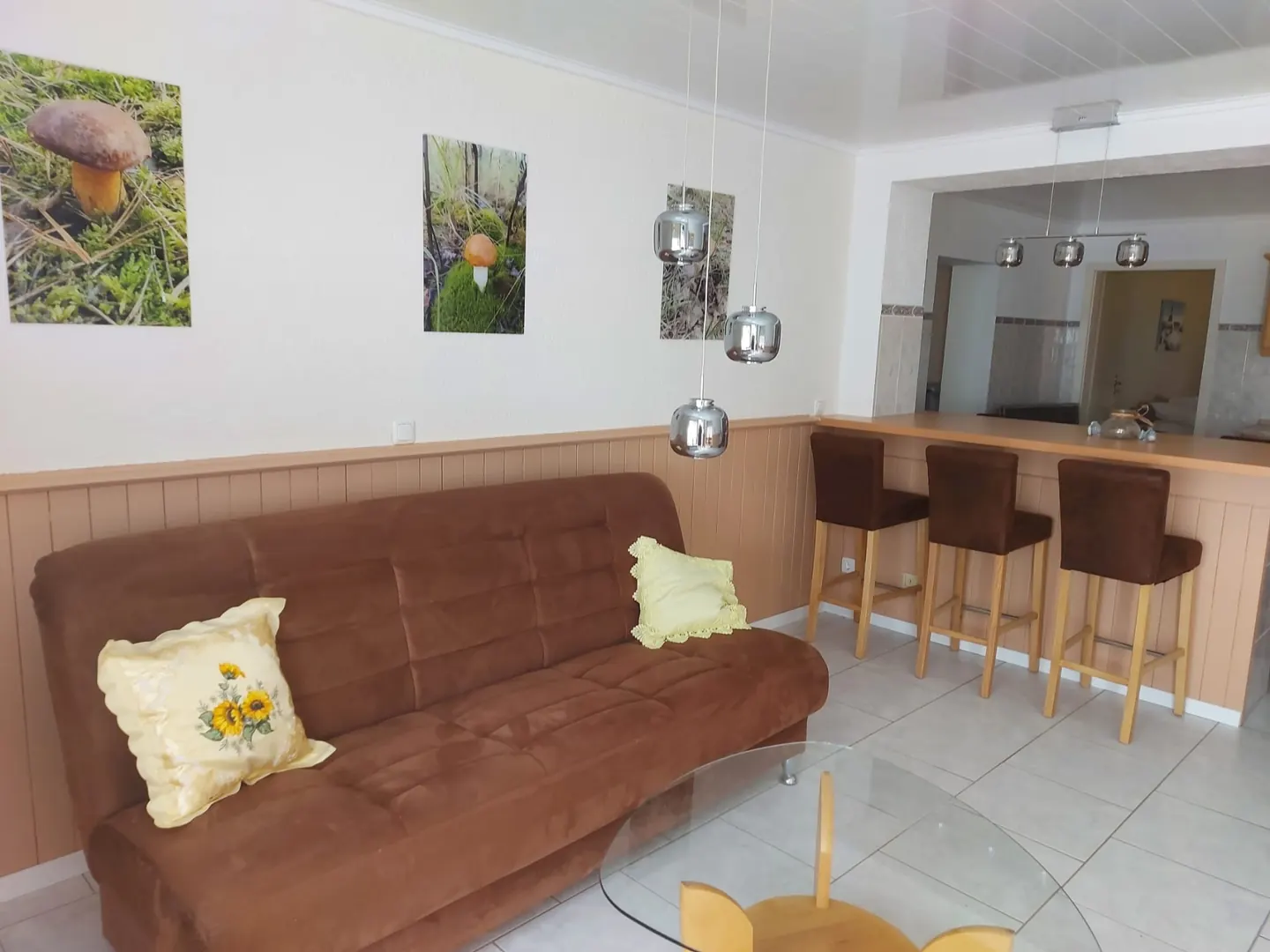 Wohnküche mit brauner Schlafcouch, Glastisch und Bartresen mit Hockern