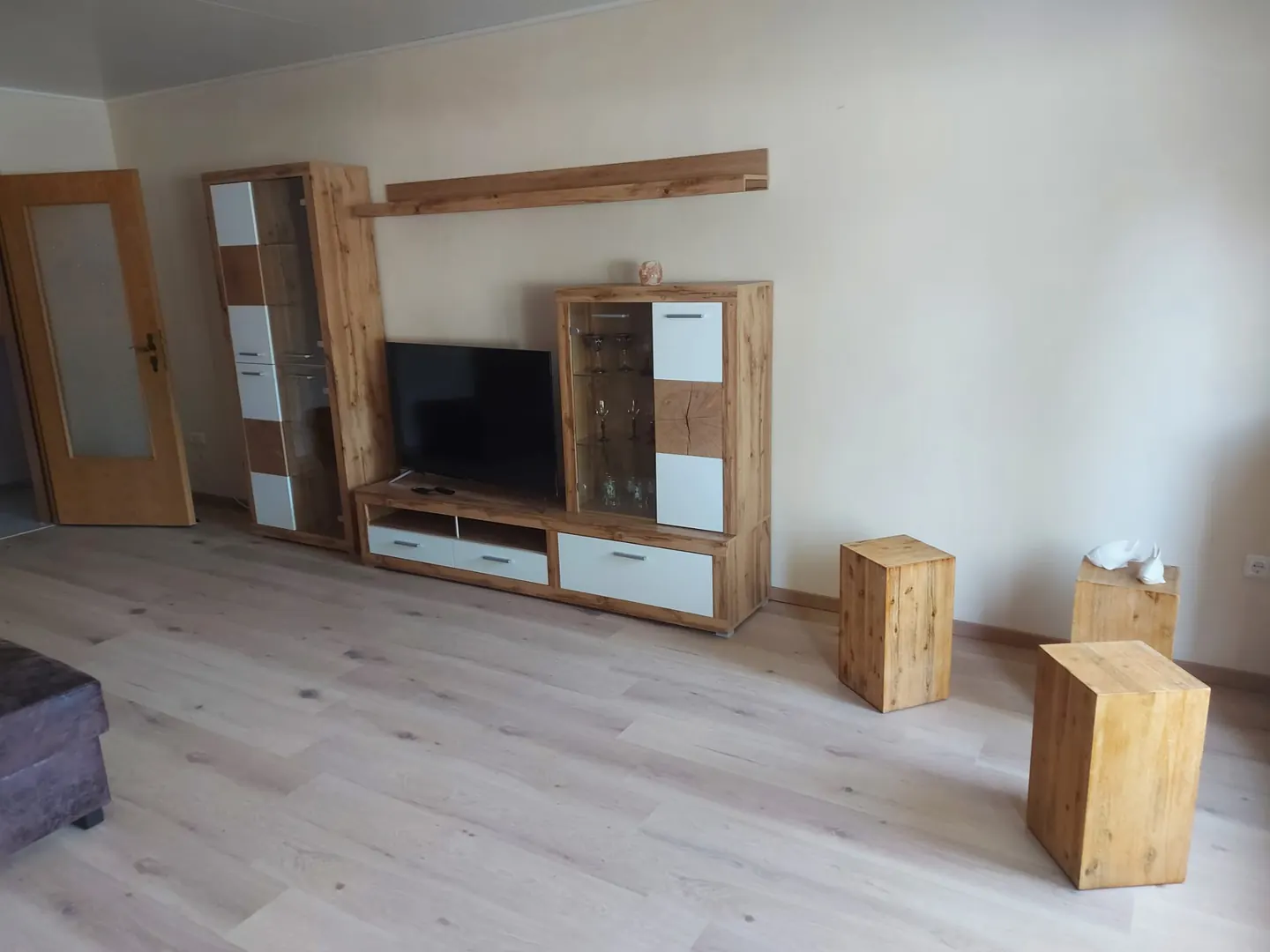 Wohnzimmer mit hellem Holzboden, Wohnwand mit Fernseher und Holzhockern