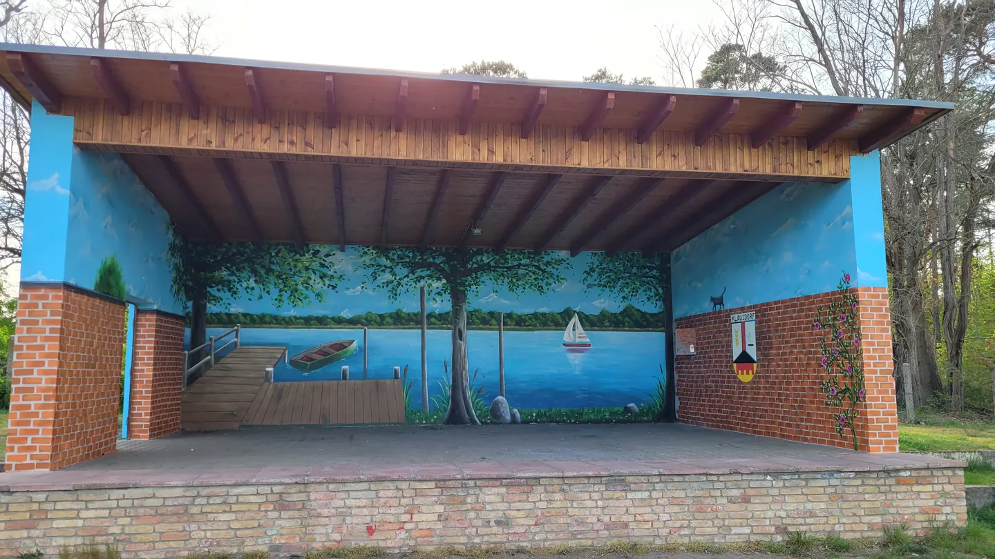Überdachte Freilichtbühne mit einem gemalten Seepanorama an der Rückwand
